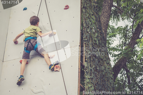 Image of little boy climbing a rock wall outdoor.