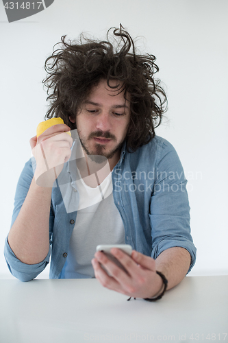 Image of young man eating apple and using a mobile phone  at home