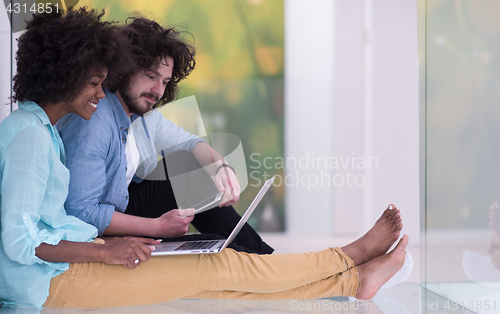 Image of multiethnic couple using a laptop on the floor
