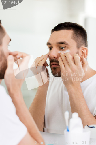 Image of young man applying cream to face at bathroom