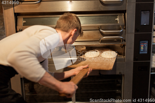 Image of baker putting dough into bread oven at bakery