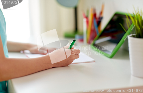 Image of girl with tablet pc writing to notebook at home