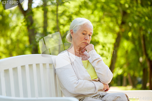 Image of sad senior woman sitting on bench at summer park