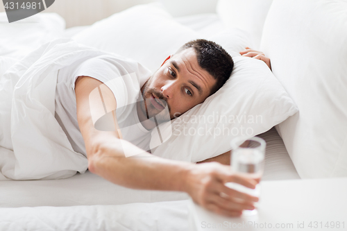 Image of man in bed and reaching to glass of water at home