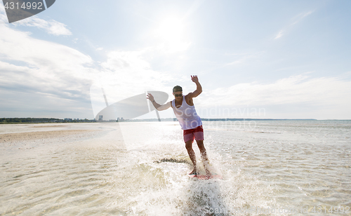 Image of young man riding on skimboard on summer beach