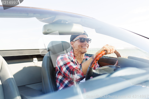 Image of happy young man driving convertible car