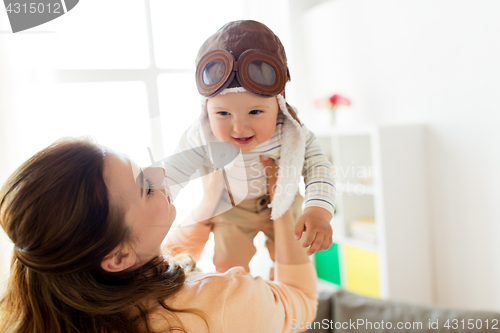 Image of happy mother with baby wearing pilot hat at home