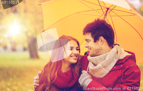 Image of smiling couple with umbrella in autumn park