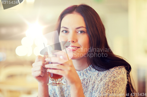 Image of smiling young woman drinking tea at cafe