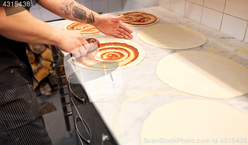 Image of cook applying tomato sauce to pizza at pizzeria