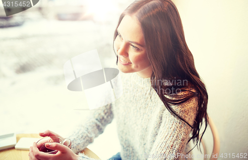 Image of smiling young woman drinking tea at cafe