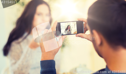 Image of man taking picture of woman by smartphone at cafe