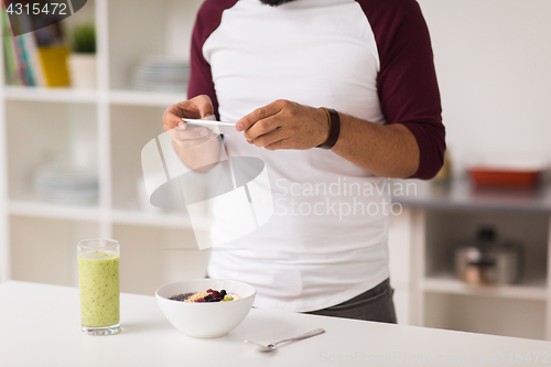 Image of man with smartphone having breakfast at home