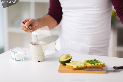 Image of man having breakfast and adding sugar to coffee