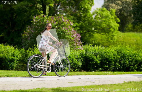 Image of happy woman riding fixie bicycle in summer park