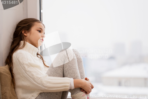 Image of sad girl sitting on sill at home window in winter