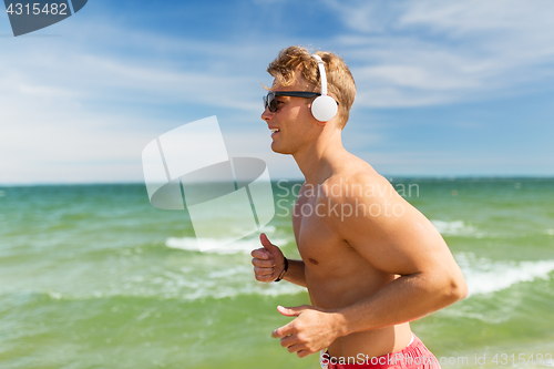 Image of happy man with headphones running along beach