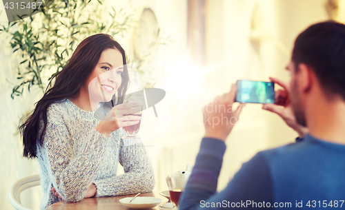 Image of man taking picture of woman by smartphone at cafe