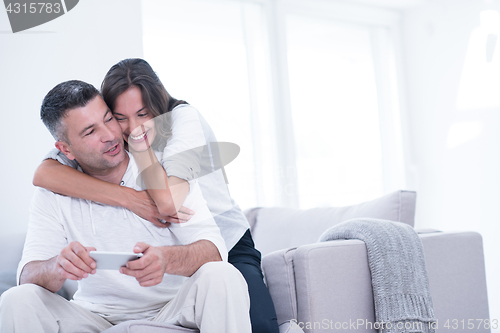 Image of happy couple using mobile phone at home