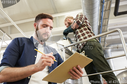 Image of men with clipboard at brewery or beer plant kettle