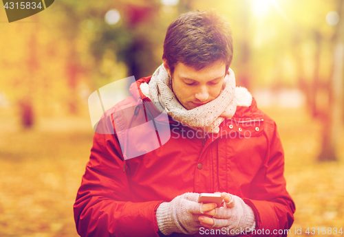 Image of young man with smartphone walking at autumn park