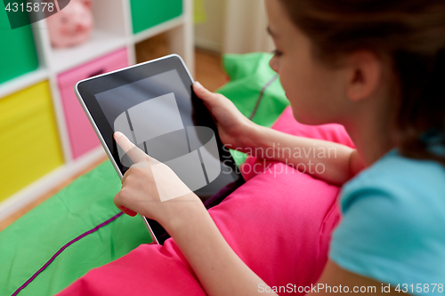 Image of smiling girl with tablet pc lying on bed at home