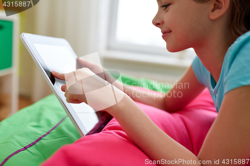 Image of smiling girl with tablet pc lying on bed at home