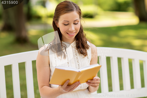 Image of smiling young woman reading book at summer park