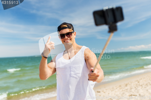 Image of man with smartphone selfie stick on summer beach