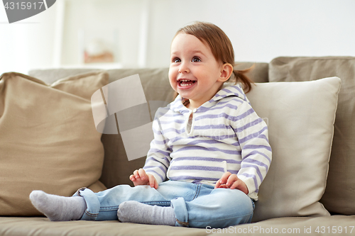 Image of happy smiling baby girl sitting on sofa at home