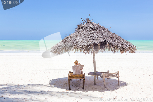 Image of Women relaxing on dack chair under wooden umbrella on tropical beach.