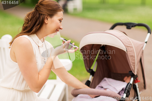 Image of happy mother with smartphone and stroller at park