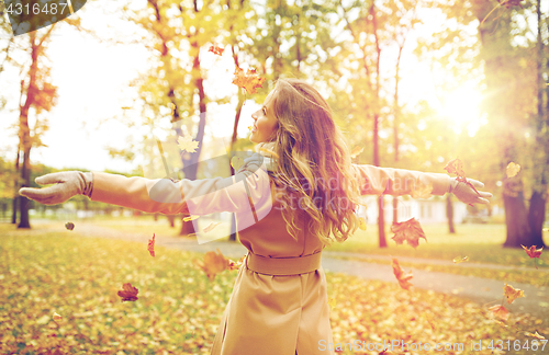 Image of happy woman having fun with leaves in autumn park