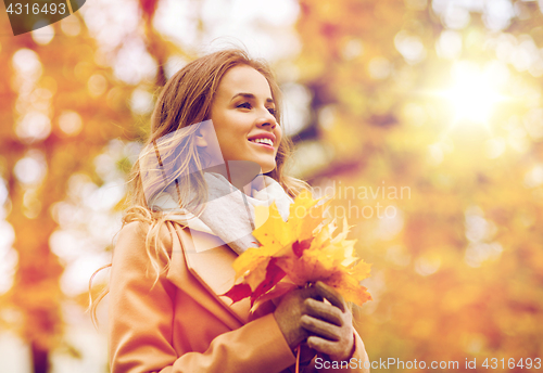 Image of beautiful woman with maple leaves in autumn park