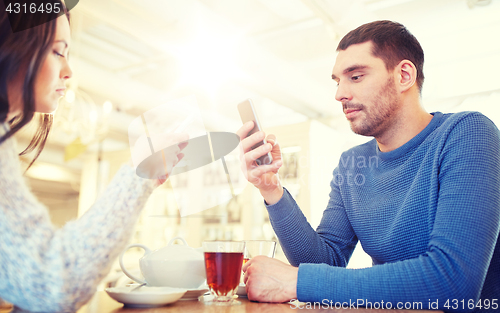 Image of couple with smartphones drinking tea at cafe