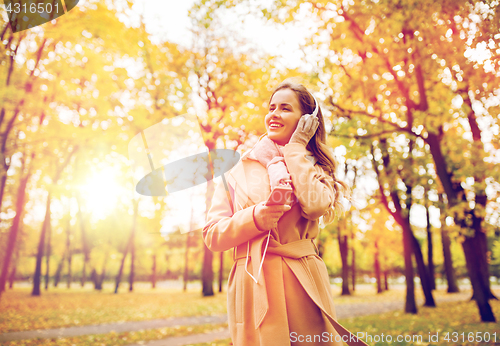 Image of woman with smartphone and earphones in autumn park