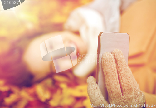 Image of woman on autumn leaves taking selfie by smartphone