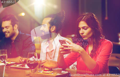 Image of woman with smartphone and friends at restaurant