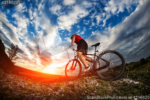 Image of cyclist riding mountain bike on rocky trail at sunrise