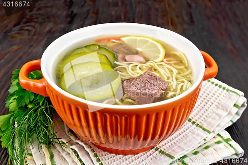 Image of Soup with zucchini and noodles in red bowl on table