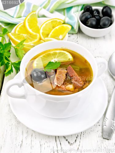 Image of Solyanka with black olives in white bowl on board