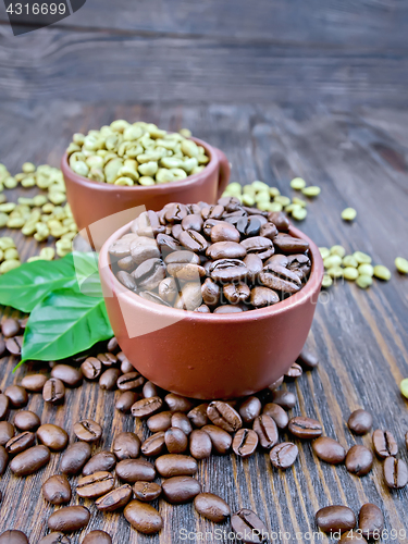 Image of Coffee black and green grains in cups with leaf on board