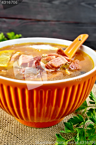 Image of Solyanka with lemon and spoon in bowl on sackcloth