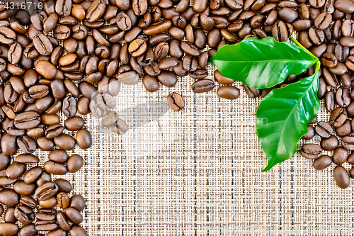 Image of Coffee black grains with leaf on brown woven fabric