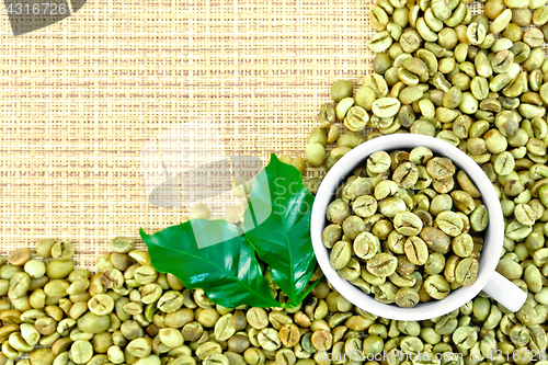 Image of Coffee green grains with cup on yellow woven fabric