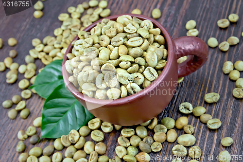 Image of Coffee green grain in cup with leaf on board