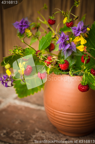 Image of Ripe strawberries and a bouquet of forest flowers in a clay mug