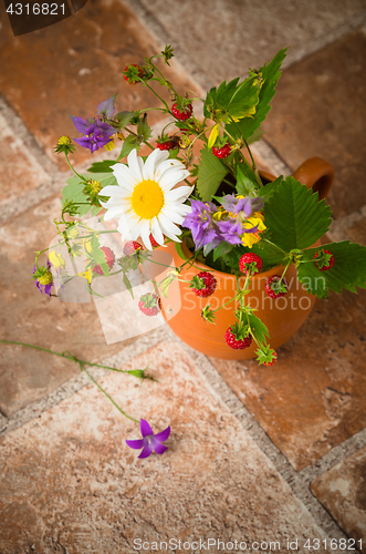 Image of Ripe strawberries and a bouquet of forest flowers in a clay mug