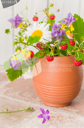 Image of Ripe strawberries and a bouquet of forest flowers in a clay mug