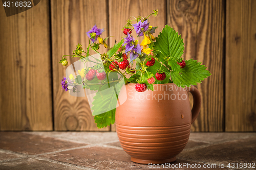 Image of Ripe strawberries and a bouquet of forest flowers in a clay mug